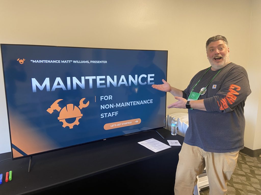 Matt standing beside a smart TV featuring the cover slide of his workshop presentation at The Great Gathering 2025.